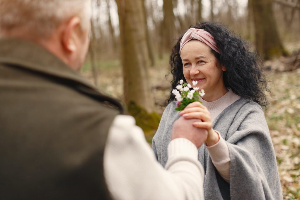 happy senior couple in love with flowers in forest