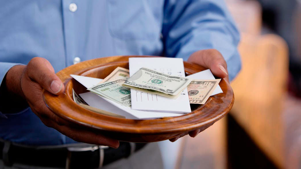 man holding collection plate filled with money and tithe envelopes